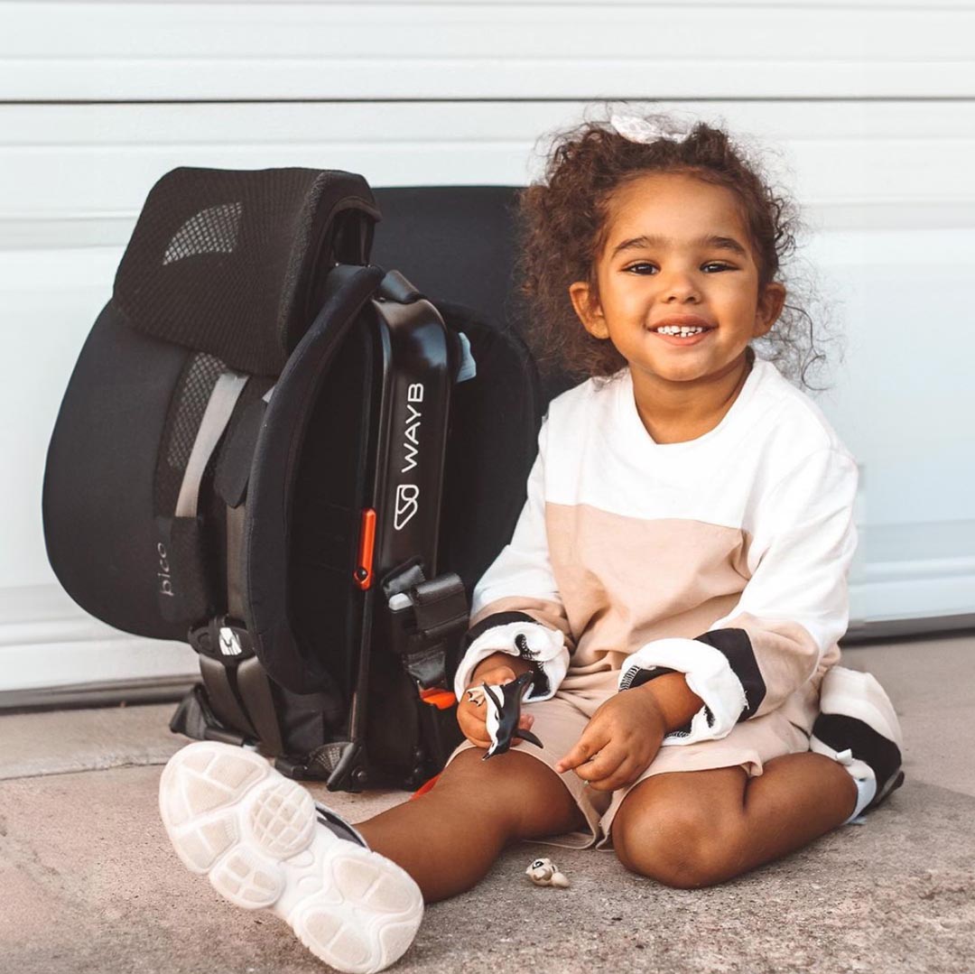 Toddler girl in front of collapsed WAYB Pico Car Seat