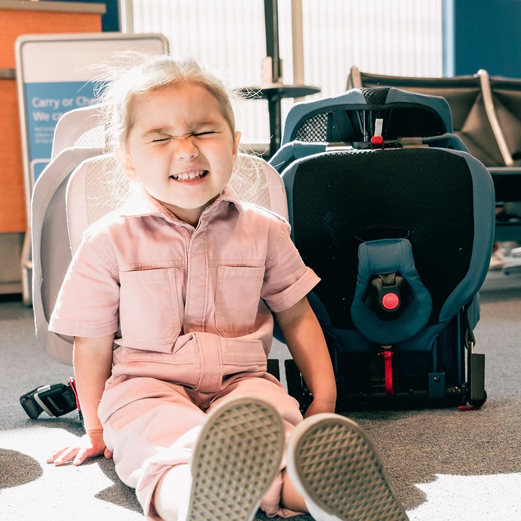 Toddler at airport in front of collapsed WAYB Pico Car Seats