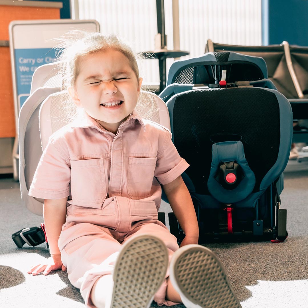 Toddler at airport in front of collapsed WAYB Pico Car Seats