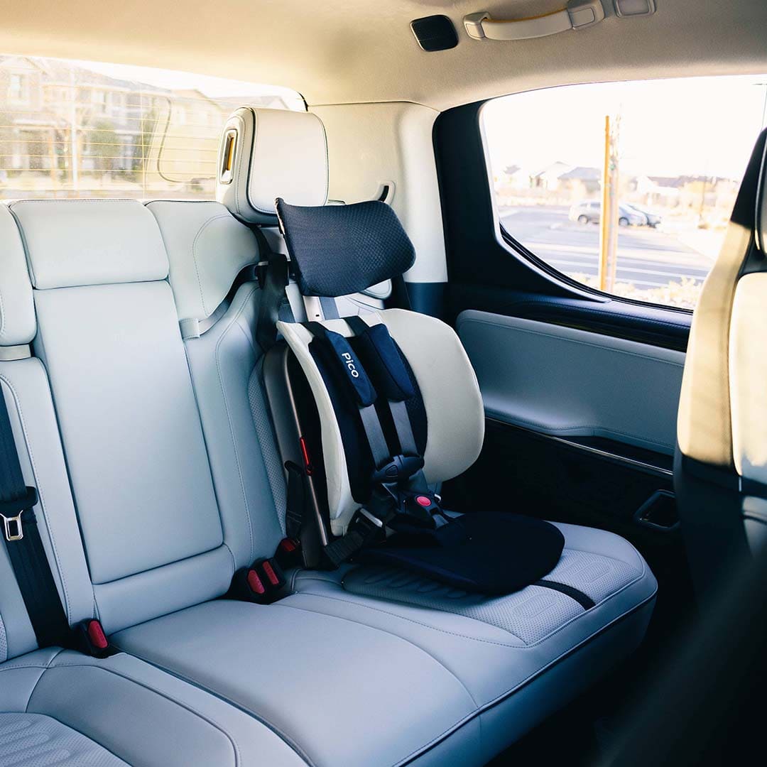 Child safety seat installed in a car's back seat with a view of the road outside.