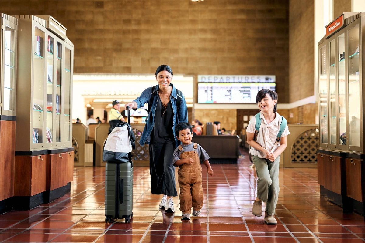 Woman with two children walking through a train station with luggage.